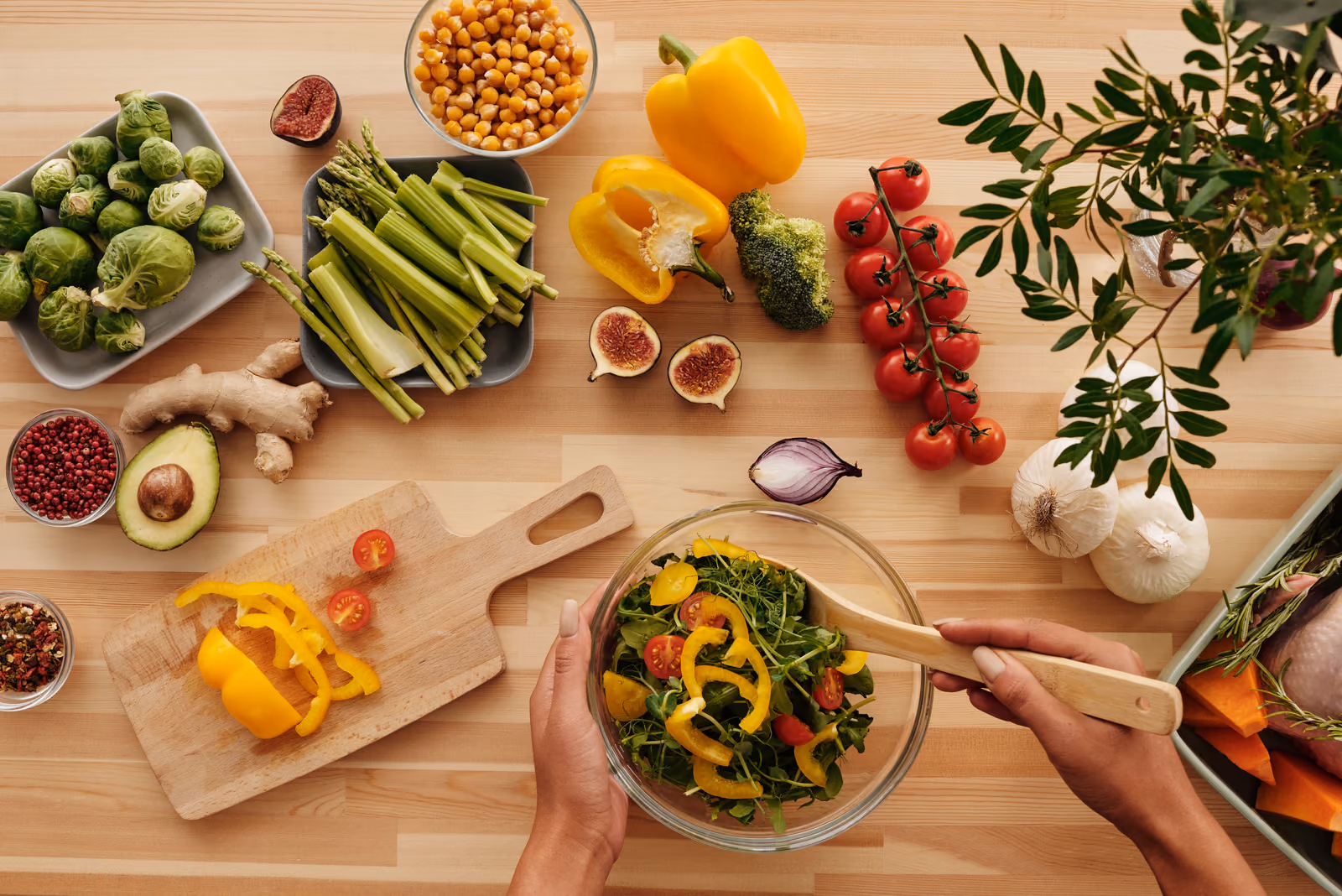 Hands tossing a colourful salad among fresh vegetables, chickpeas and herbs on a wooden table
